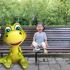 男孩坐在卡通恐龙旁边公园长椅上:男孩坐在卡通恐龙旁边公园长凳上